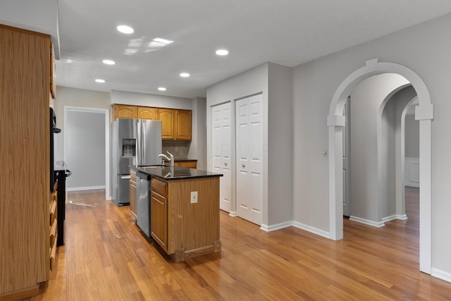 kitchen featuring decorative backsplash, light wood-type flooring, a kitchen island with sink, and stainless steel appliances