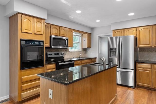 kitchen featuring sink, light hardwood / wood-style floors, decorative backsplash, a center island with sink, and appliances with stainless steel finishes