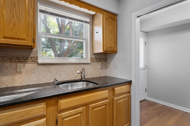 kitchen featuring backsplash, dark hardwood / wood-style floors, dark stone countertops, and sink