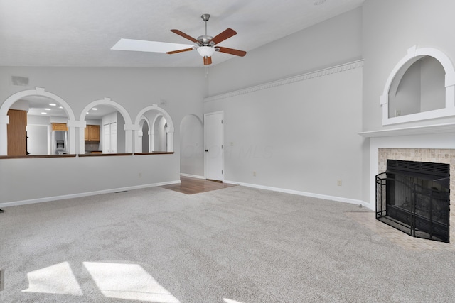 unfurnished living room featuring carpet, high vaulted ceiling, a tile fireplace, and ceiling fan