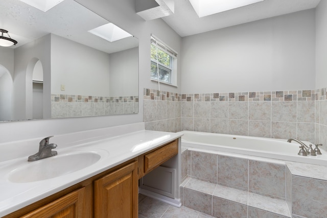 bathroom with tile patterned flooring, vanity, a relaxing tiled tub, and a skylight