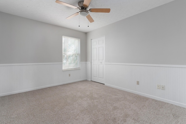 carpeted spare room featuring a textured ceiling, ceiling fan, and wood walls