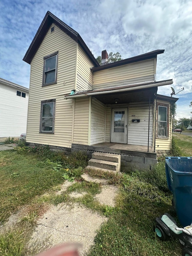 rear view of property featuring a lawn and covered porch