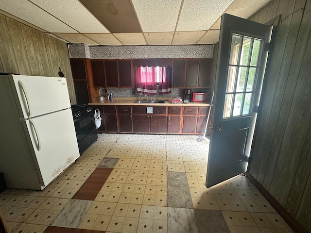 kitchen featuring black appliances, a paneled ceiling, sink, and wooden walls