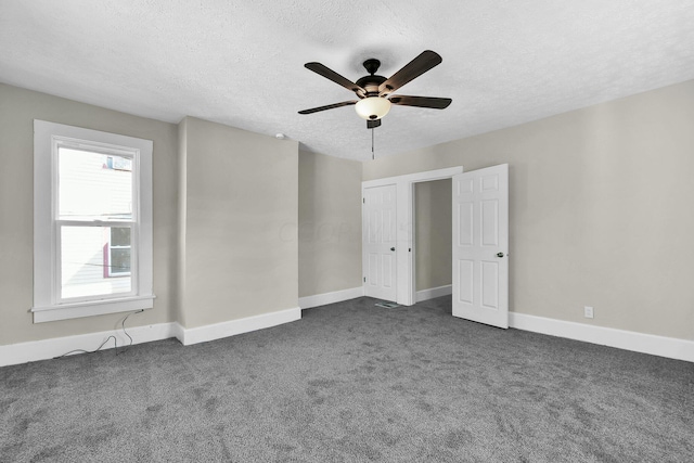 unfurnished room with ceiling fan, dark carpet, and a textured ceiling