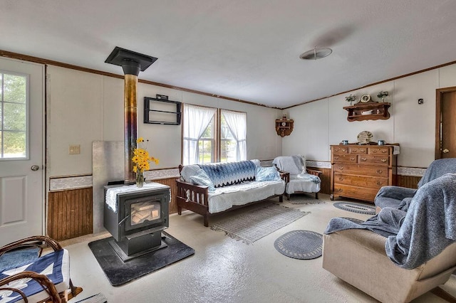 living room featuring a wood stove, wooden walls, plenty of natural light, and ornamental molding