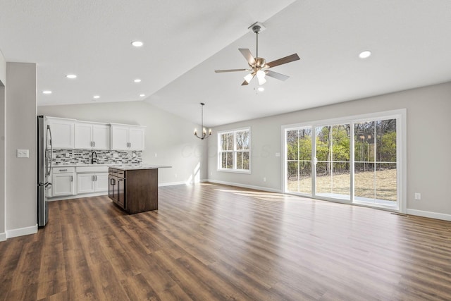 unfurnished living room with ceiling fan with notable chandelier, sink, dark hardwood / wood-style flooring, and vaulted ceiling