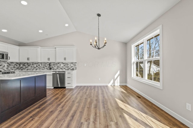 kitchen with lofted ceiling, white cabinets, pendant lighting, stainless steel appliances, and backsplash