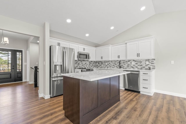 kitchen with tasteful backsplash, vaulted ceiling, hanging light fixtures, appliances with stainless steel finishes, and white cabinets