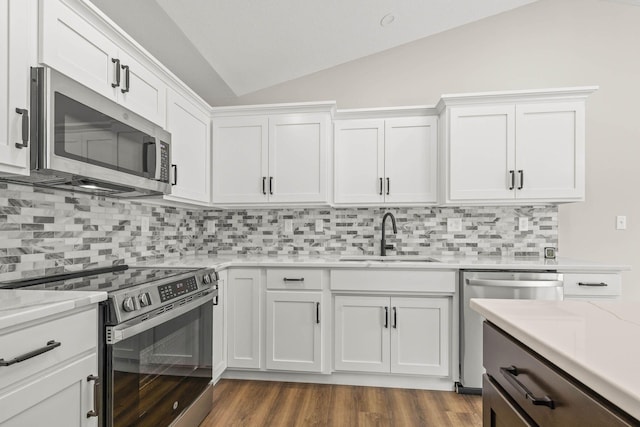 kitchen featuring stainless steel appliances, vaulted ceiling, sink, and white cabinetry