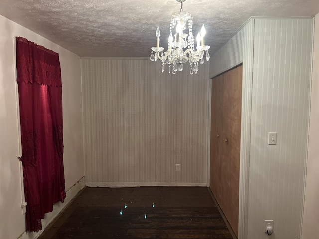 spare room with a textured ceiling, dark hardwood / wood-style floors, and a notable chandelier