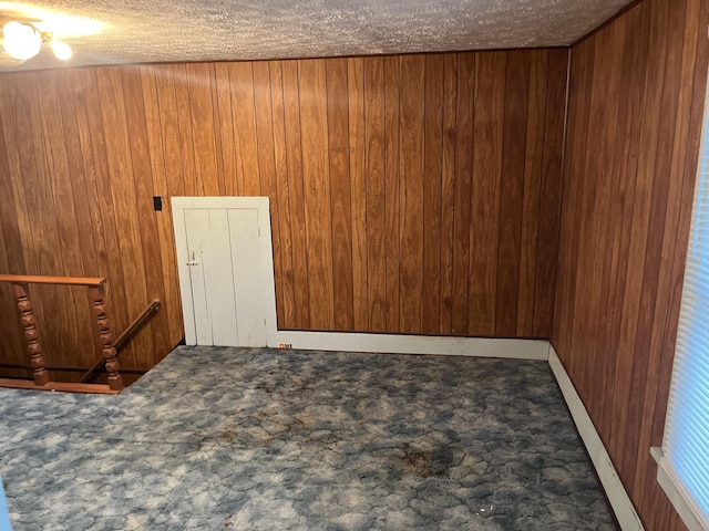 carpeted spare room with wood walls and a textured ceiling