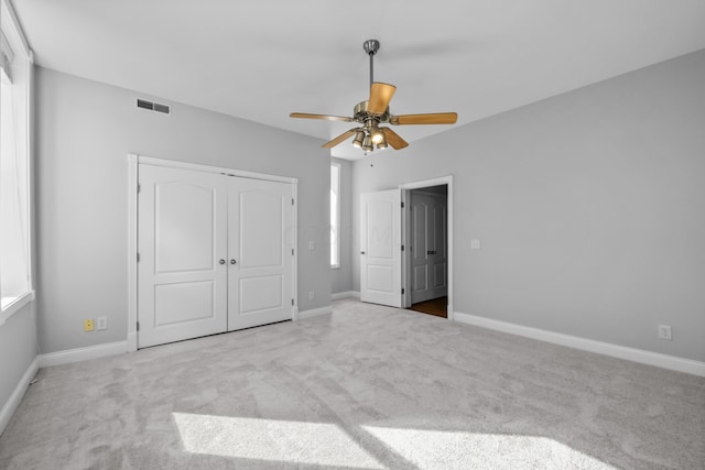 unfurnished bedroom with ceiling fan, a closet, light colored carpet, and multiple windows