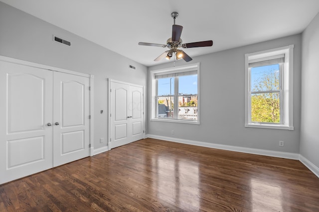 unfurnished bedroom with ceiling fan, dark wood-type flooring, and multiple closets