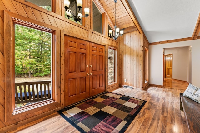 foyer with wooden walls, hardwood / wood-style floors, high vaulted ceiling, and an inviting chandelier