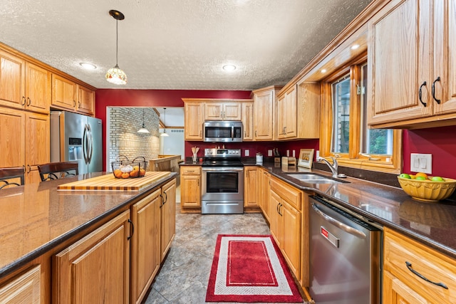 kitchen with a textured ceiling, stainless steel appliances, sink, pendant lighting, and dark stone countertops