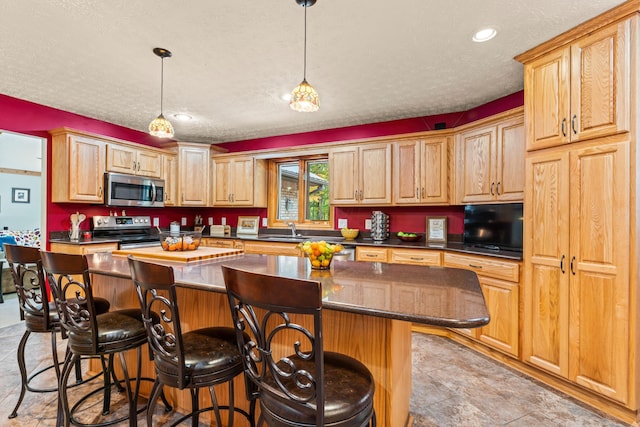 kitchen featuring a textured ceiling, a center island, stainless steel appliances, and a breakfast bar area