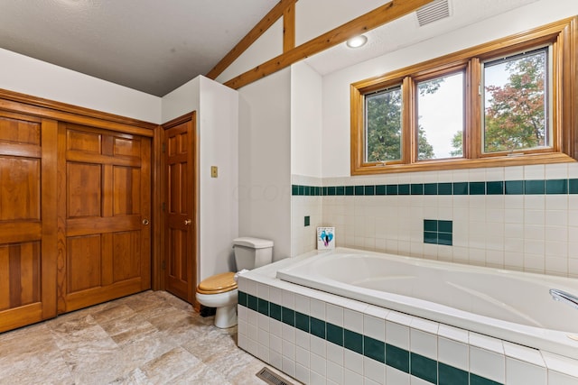 bathroom featuring a textured ceiling, a relaxing tiled tub, toilet, and lofted ceiling