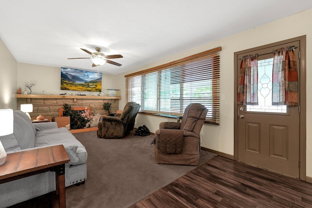 living room with ceiling fan, a healthy amount of sunlight, a stone fireplace, and dark wood-type flooring