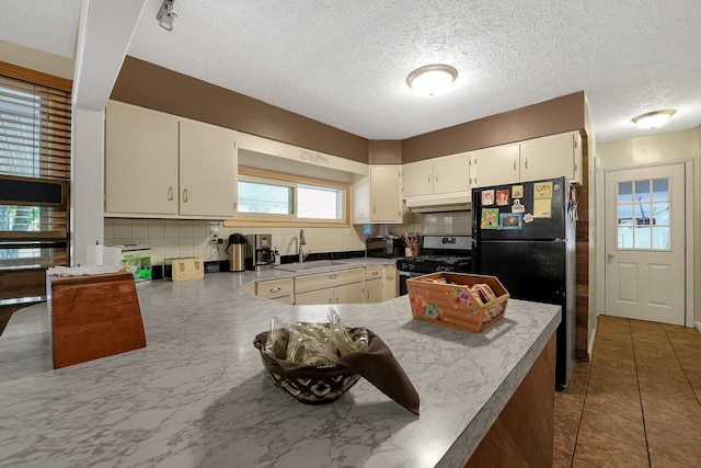 kitchen featuring stainless steel gas stove, sink, black fridge, kitchen peninsula, and decorative backsplash