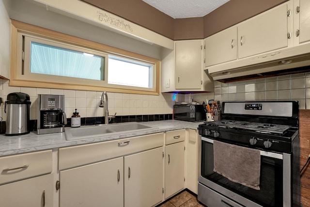 kitchen with a textured ceiling, decorative backsplash, gas stove, and sink