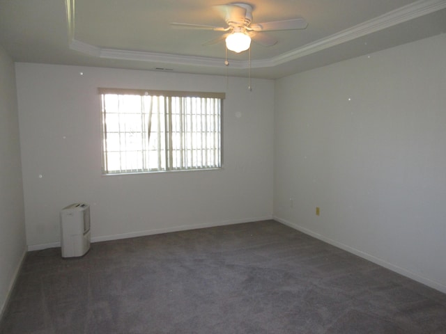 unfurnished room with a raised ceiling, ceiling fan, ornamental molding, and dark colored carpet