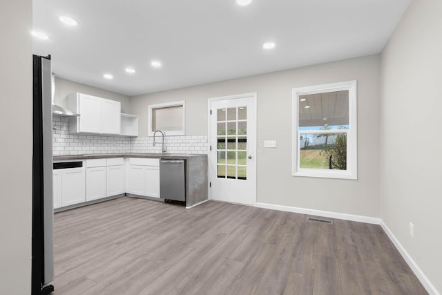 kitchen featuring backsplash, white cabinetry, stainless steel dishwasher, and light hardwood / wood-style flooring