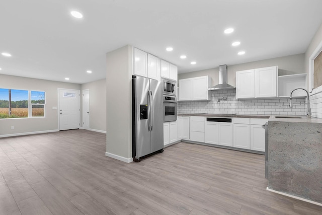 kitchen featuring wall chimney range hood, sink, light wood-type flooring, white cabinetry, and stainless steel appliances