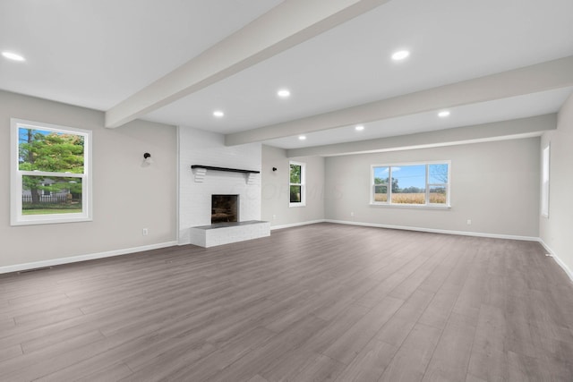 unfurnished living room featuring a fireplace, plenty of natural light, beamed ceiling, and light hardwood / wood-style floors