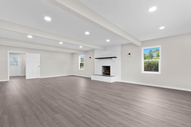 unfurnished living room featuring plenty of natural light, beam ceiling, wood-type flooring, and a fireplace