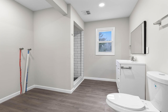 bathroom featuring hardwood / wood-style floors, vanity, toilet, and a tile shower