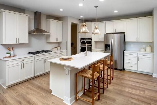 kitchen featuring light wood-style flooring, white cabinetry, stainless steel appliances, wall chimney exhaust hood, and light countertops