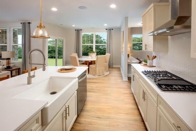 kitchen with light wood finished floors, wall chimney range hood, decorative light fixtures, gas cooktop, and a sink