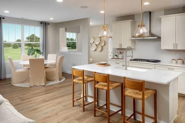 kitchen with an island with sink, wall chimney range hood, a kitchen breakfast bar, light wood finished floors, and light countertops