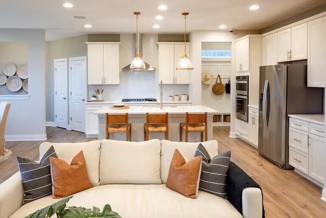 kitchen featuring stainless steel appliances, a kitchen island with sink, light countertops, and wall chimney range hood