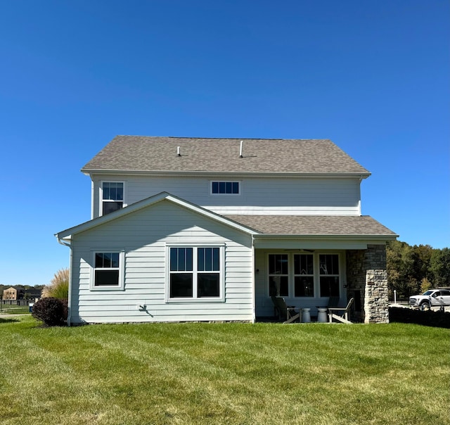 back of property featuring a shingled roof and a yard