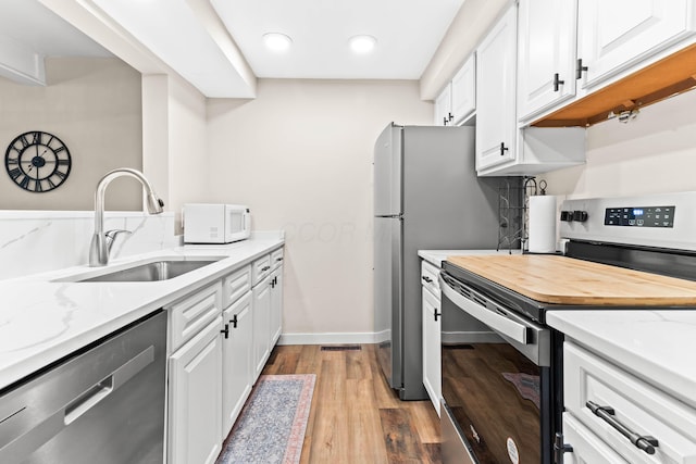 kitchen with light stone counters, stainless steel appliances, sink, wood-type flooring, and white cabinets