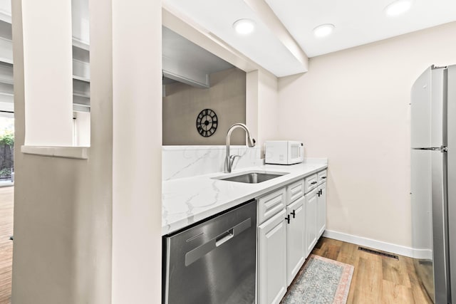 kitchen with light wood-type flooring, light stone counters, stainless steel appliances, sink, and white cabinetry