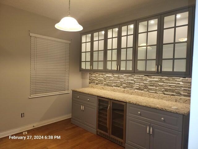 bar featuring light stone countertops, backsplash, decorative light fixtures, and beverage cooler