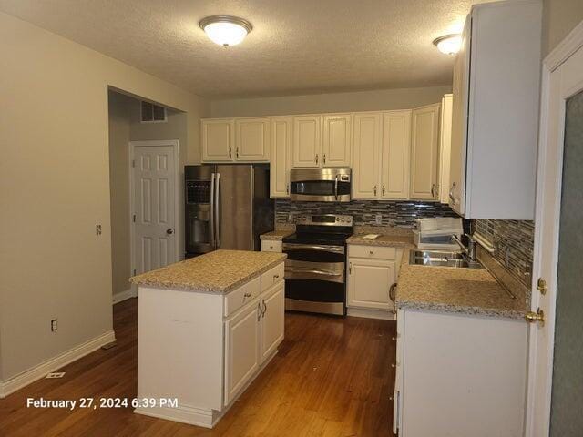 kitchen featuring a textured ceiling, stainless steel appliances, sink, white cabinets, and a center island