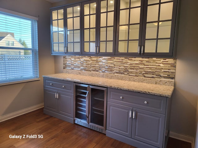 bar with decorative backsplash, dark hardwood / wood-style floors, light stone counters, and beverage cooler