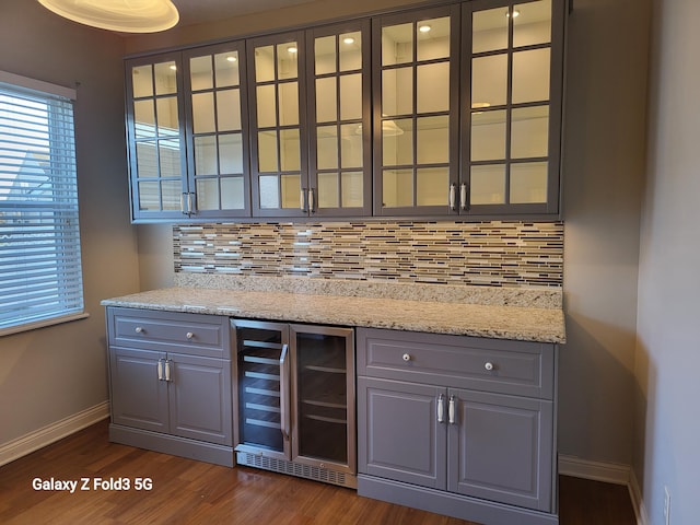 bar with light stone counters, decorative backsplash, beverage cooler, and dark hardwood / wood-style floors