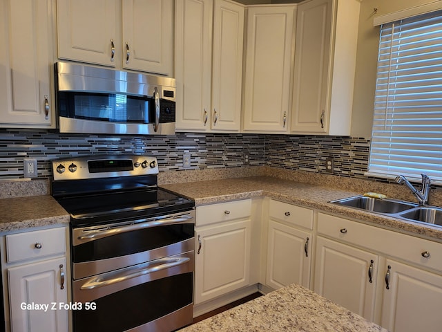 kitchen with decorative backsplash, white cabinetry, sink, and appliances with stainless steel finishes