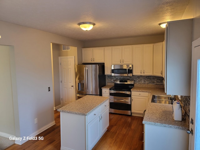 kitchen with dark hardwood / wood-style flooring, stainless steel appliances, sink, white cabinetry, and a kitchen island