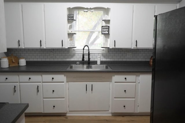 kitchen with backsplash, black fridge, sink, and white cabinets