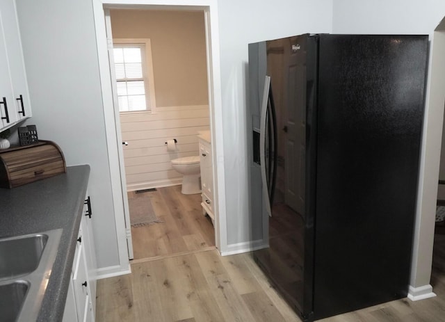 kitchen with white cabinetry, sink, wood walls, light hardwood / wood-style floors, and black fridge with ice dispenser