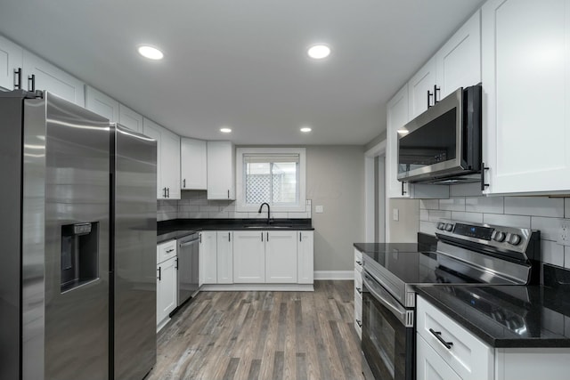 kitchen with appliances with stainless steel finishes, tasteful backsplash, sink, white cabinets, and hardwood / wood-style floors