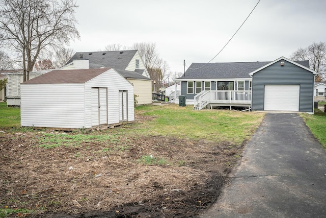 rear view of property with a garage, covered porch, a yard, and an outbuilding