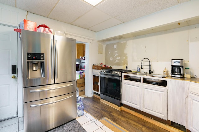 kitchen with a paneled ceiling, white cabinets, stainless steel appliances, and hardwood / wood-style flooring