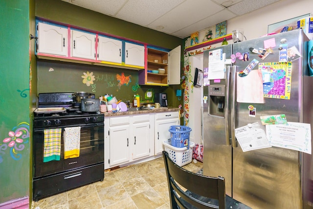 kitchen with stainless steel fridge, gas stove, white cabinetry, and a paneled ceiling